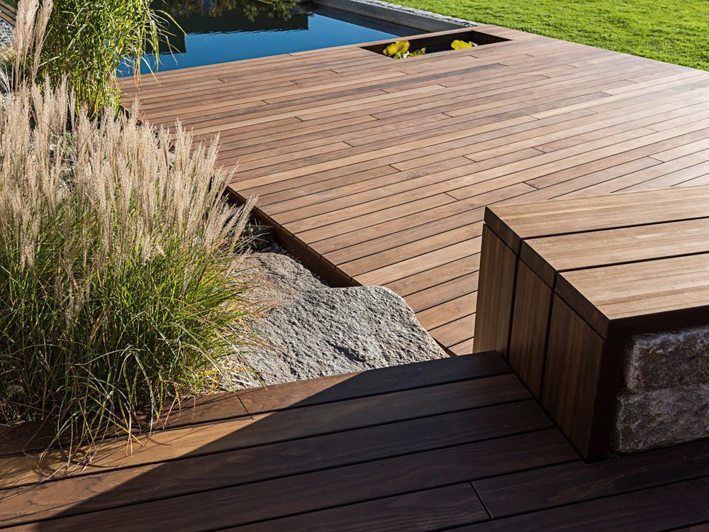 Holzterrasse mit eingebauter Bank, neben einem Pool und Zierrasen.