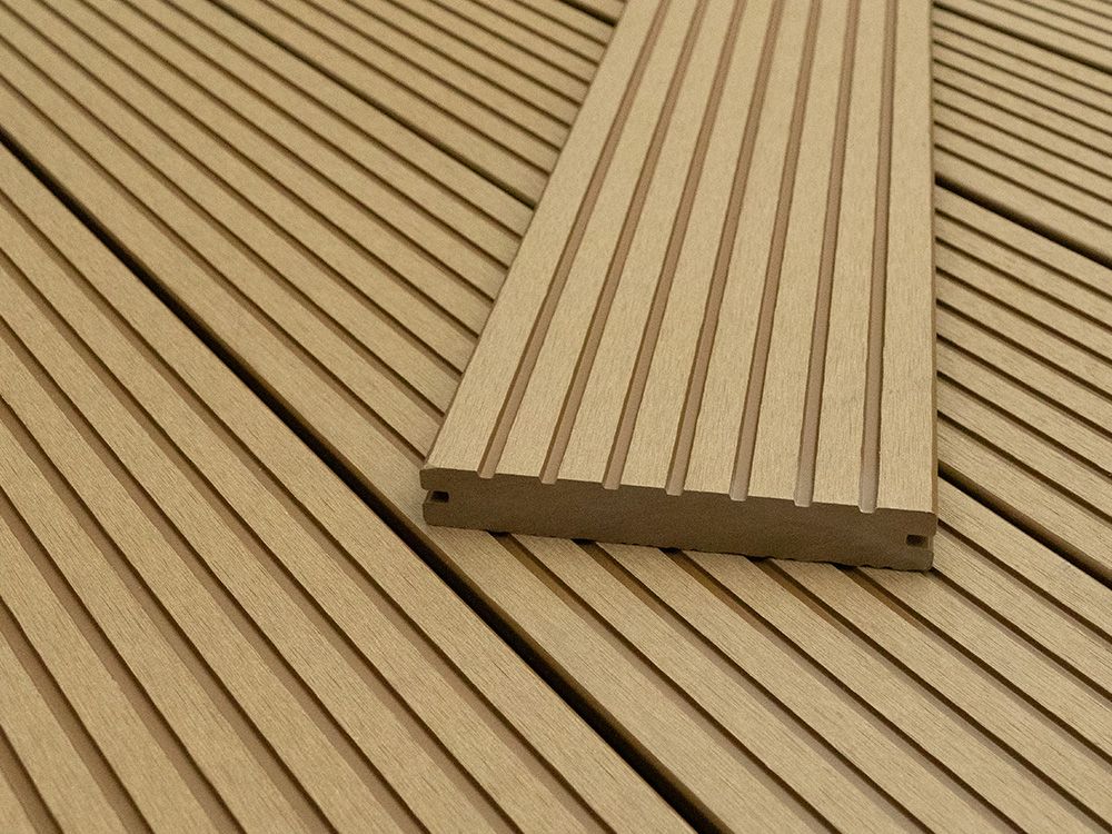 Beigefarbene Terrassendielen aus Verbundmaterial mit Rillen, eine Diele teilweise angehoben, im Außenbereich aufgestellt.