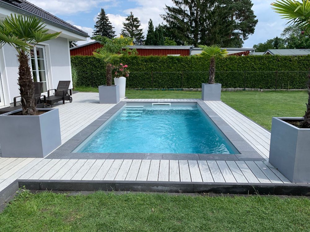 Der Hinterhofpool ist von einer hellgrauen Terrasse mit Palmen in Pflanzkübeln umgeben.