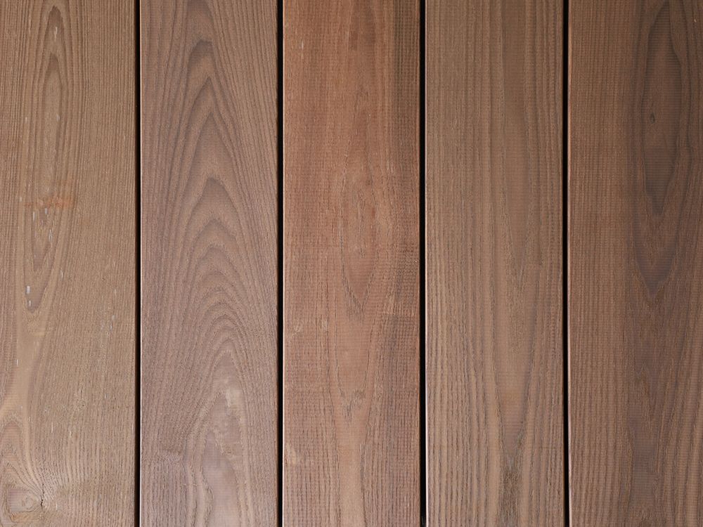 Nahaufnahme von senkrechten Holzplanken mit unterschiedlichen Brauntönen und sichtbarer Holzmaserung.