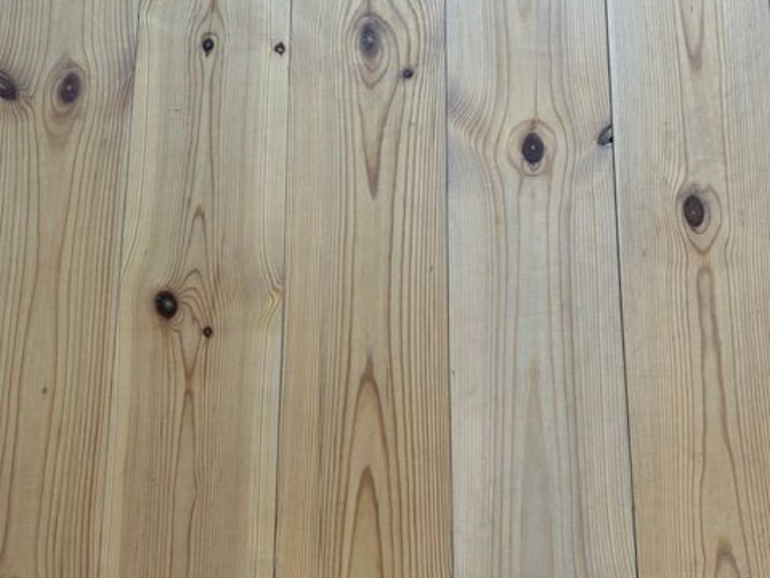 Eine helle Holztischplatte mit sichtbarer Maserung steht mittig auf einem gefliesten Boden.