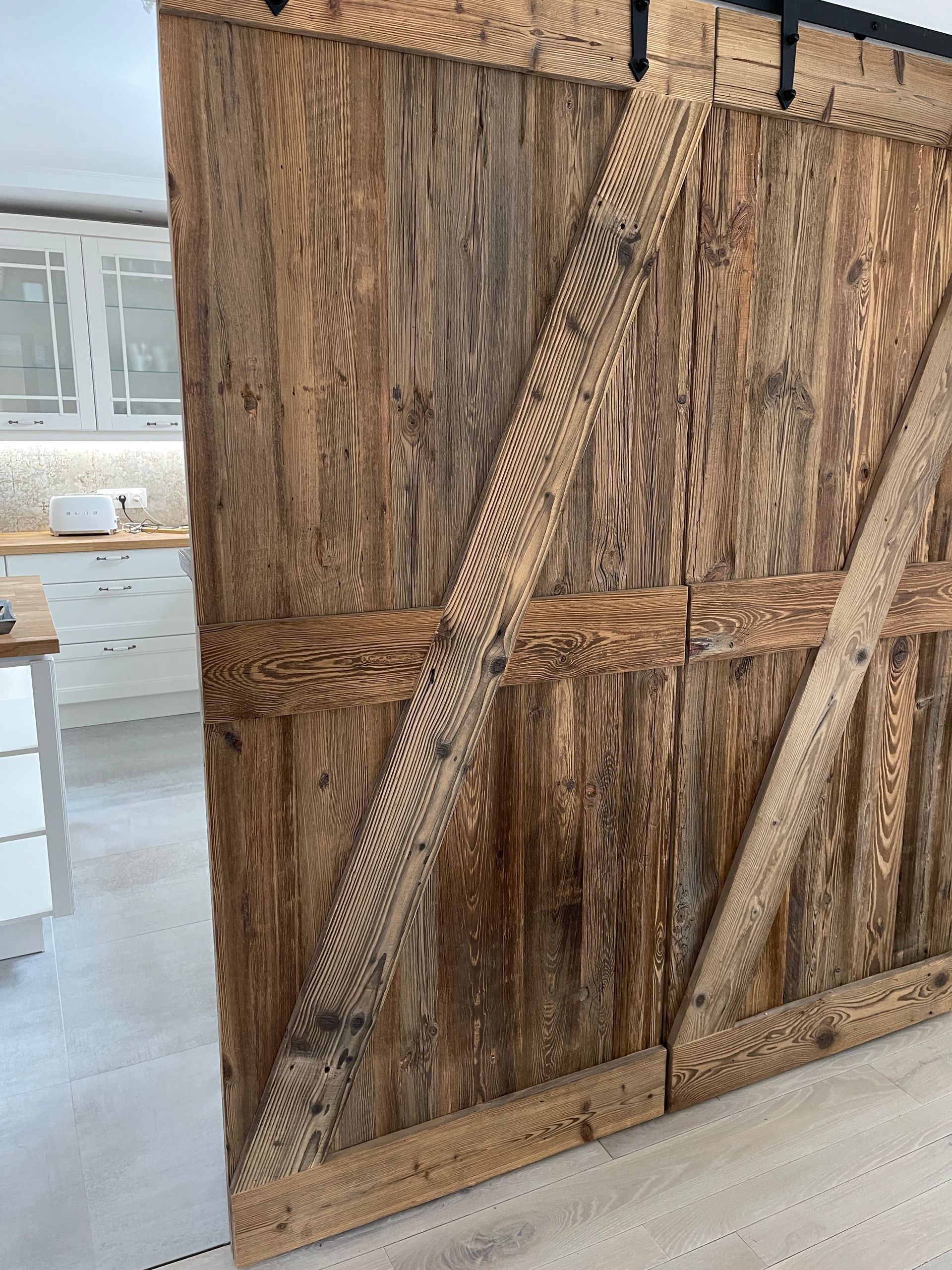 Rustikale, doppelte Scheunentüren aus Holz mit diagonalen Querverstrebungen und strukturierter Maserung, eingebaut in einem hellen Raum.