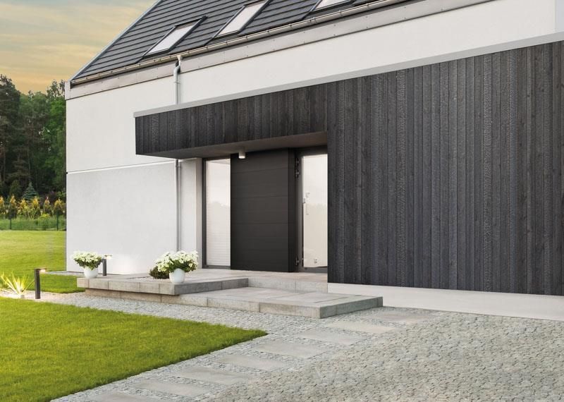 Die Vorderseite eines modernen Hauses mit einer schwarzen Tür und einem dorthin führenden Gehweg.