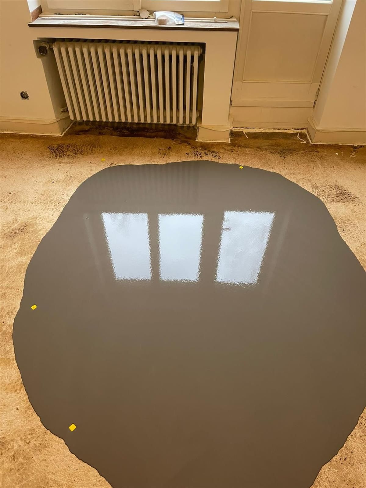 Eine große Wasserpfütze auf dem Boden in einem Raum mit einem Heizkörper.
