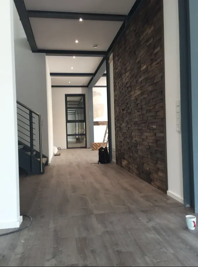 Innenansicht eines modernen Flurs mit dunklem Holzboden, einer Akzentwand aus Ziegelsteinen und freiliegenden Deckenbalken.