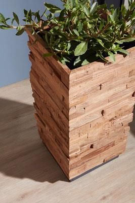 Ein hölzerner Blumentopf mit einer Pflanze darin steht auf einem Holzboden.