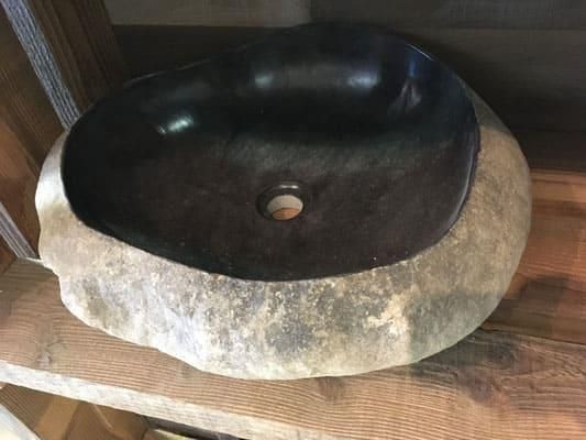 Auf einem Holzregal steht ein schwarzes Steinwaschbecken.