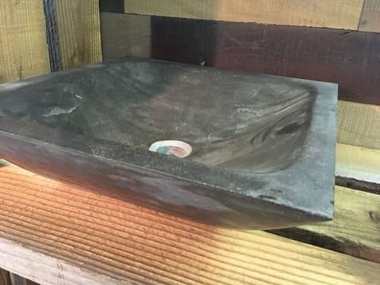 Auf einem Holzregal steht ein schwarzes Steinwaschbecken.