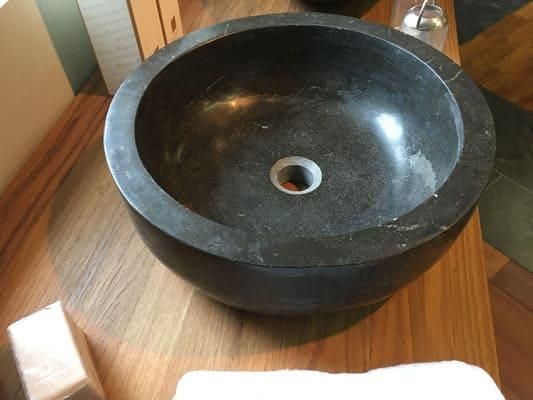 Auf einer Holztheke steht ein schwarzes Steinwaschbecken.