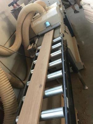 Eine Maschine schneidet ein Stück Holz auf einem Förderband.