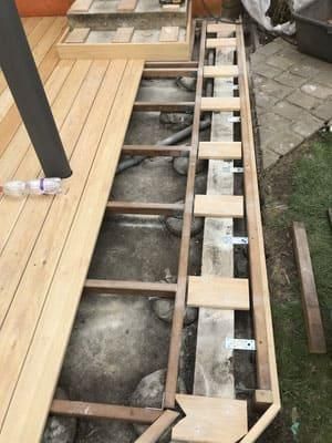 Auf einem gepflasterten Gehweg wird ein Holzdeck gebaut.