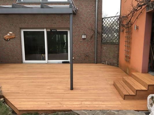 Eine Holzterrasse mit Treppe vor einem Backsteingebäude.
