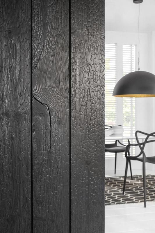 Eine schwarze Holztür führt zu einem Esszimmer mit Tisch und Stühlen.