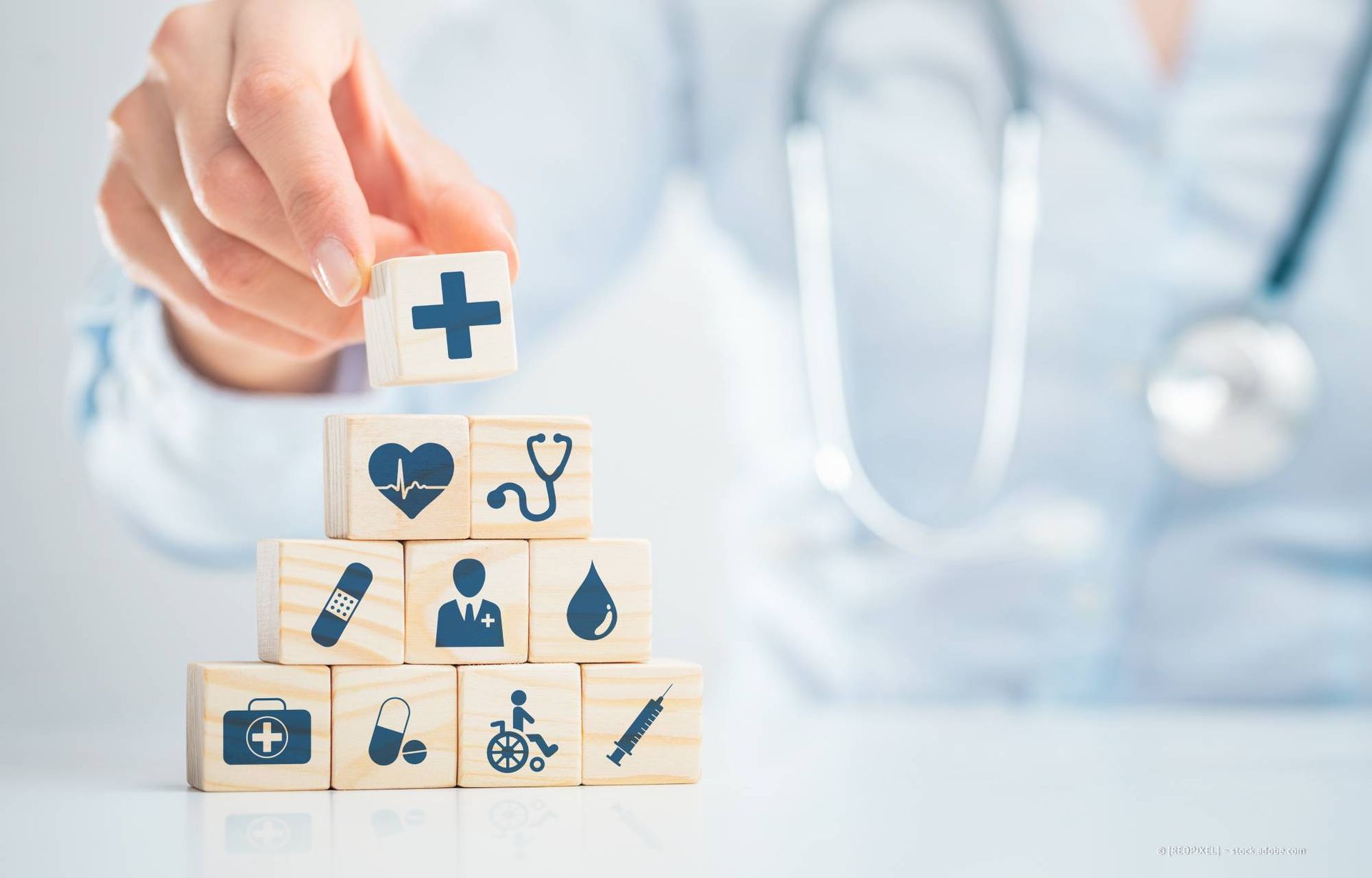 Ein Arzt stapelt Holzklötze mit Symbolen aus dem Gesundheitswesen.