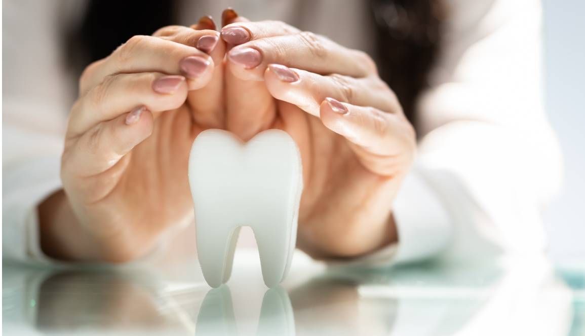 Hände, die einen weißen Zahn umschließen, symbolisieren Zahnschutz und Zahnpflege.