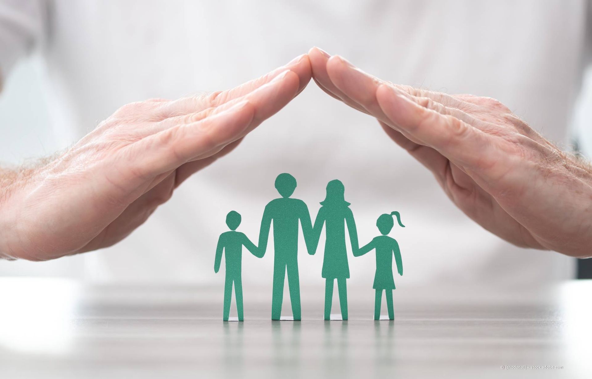 Hände, die eine ausgeschnittene Papierfamilie schützen, symbolisieren Schutz.