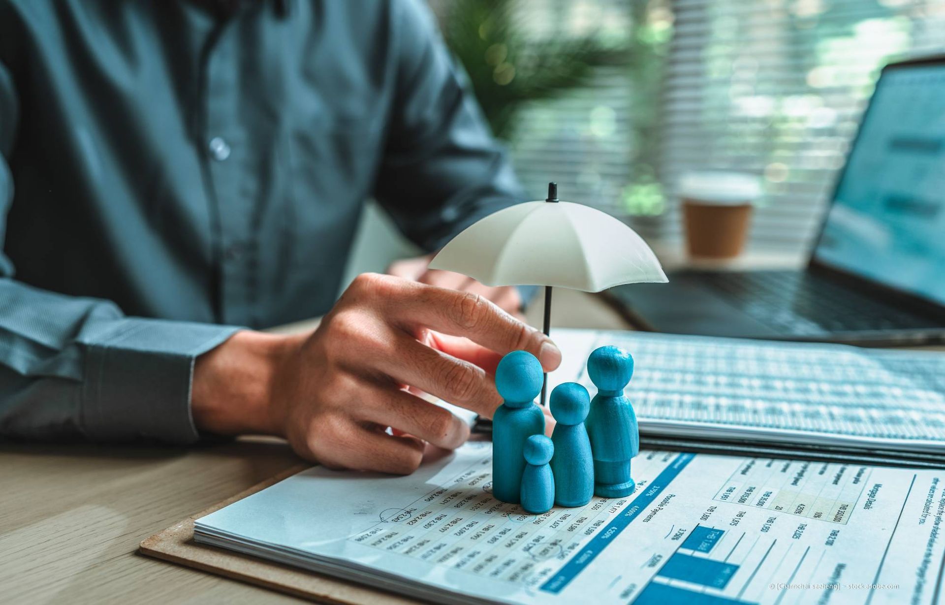 Eine Person schützt eine Familienfigur mit einem kleinen Regenschirm, was auf eine Art Versicherung hindeutet.