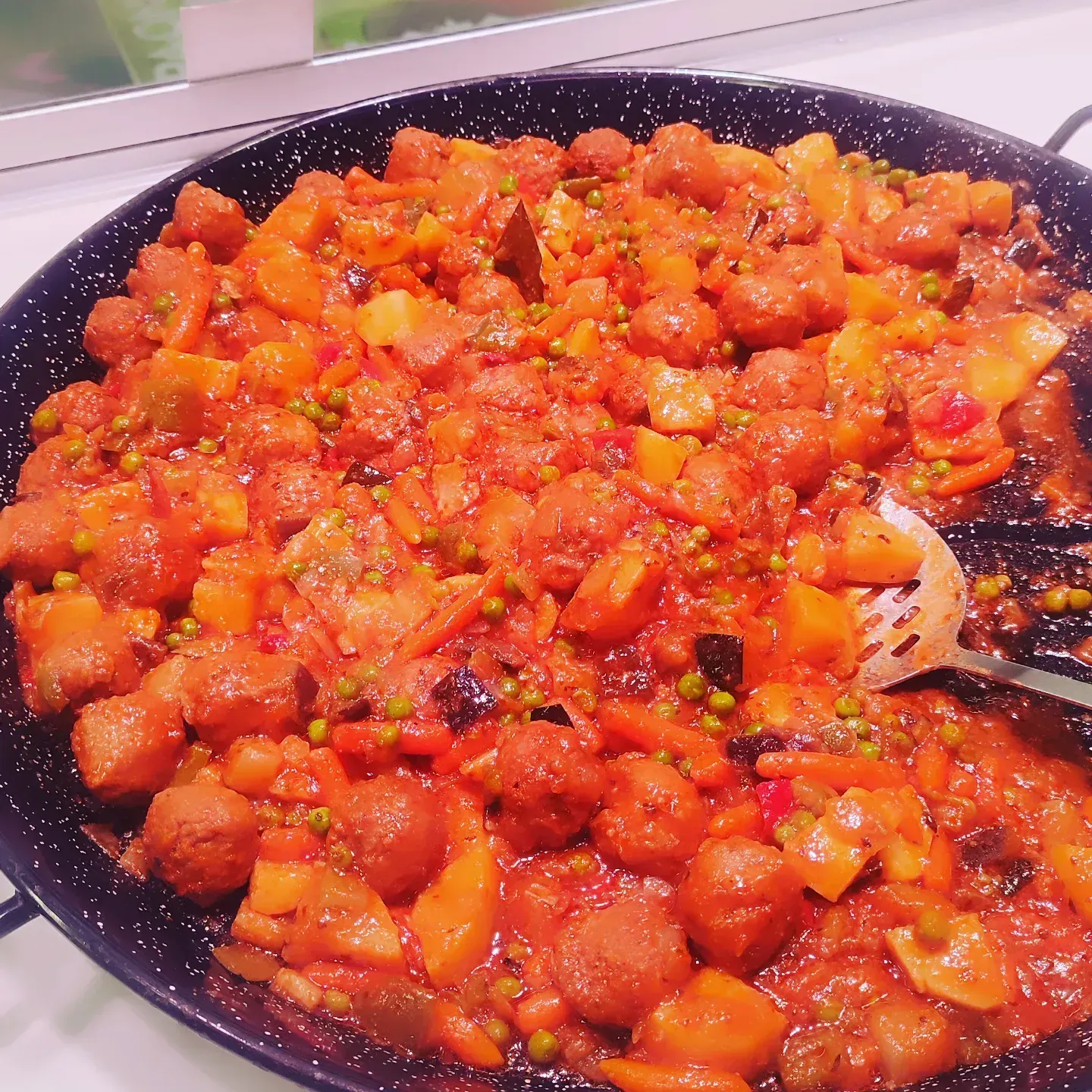 Sartén con verduras o carne picada en salsa roja y una cuchara para servir.