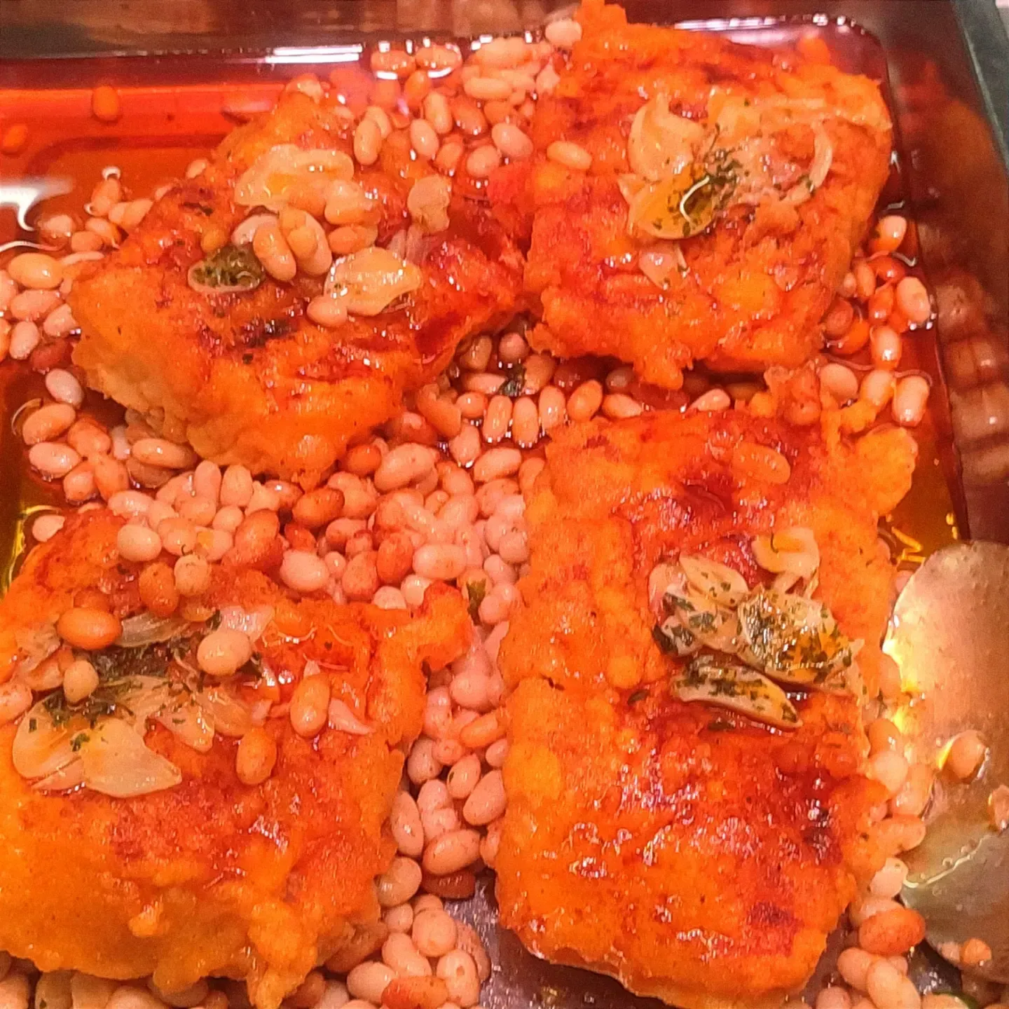 Cuatro trozos de naranja fritos cubiertos con hierbas sobre judías rosas en una bandeja.