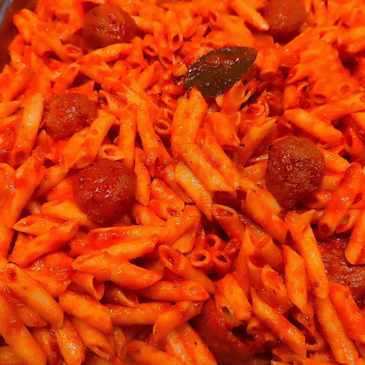 Pasta penne roja con salsa de tomate y una hoja de albahaca encima.