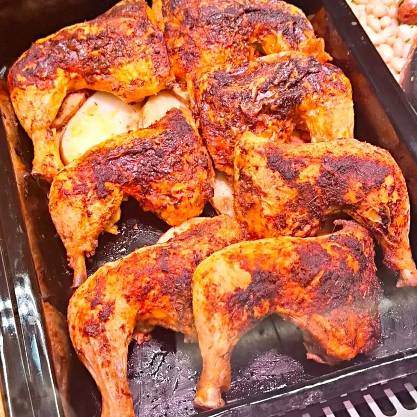 Pollos enteros asados ​​en una bandeja, dorados y chamuscados, con patatas en una esquina.