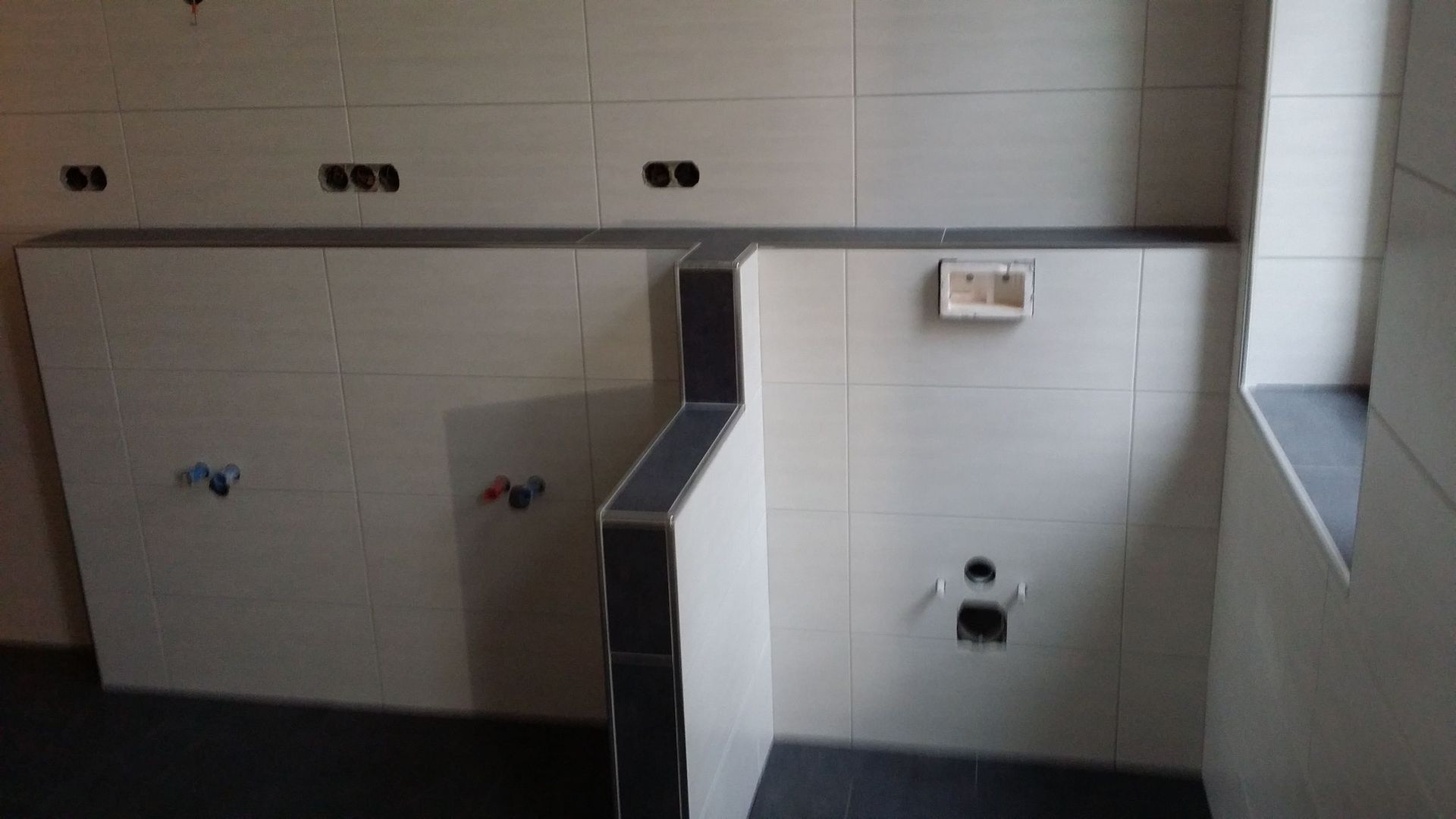 Ein Badezimmer mit weißen Fliesen und schwarzem Boden.