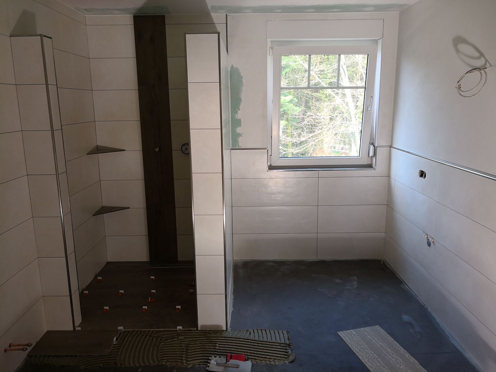 Ein im Bau befindliches Badezimmer mit weißen Fliesen und einem Fenster