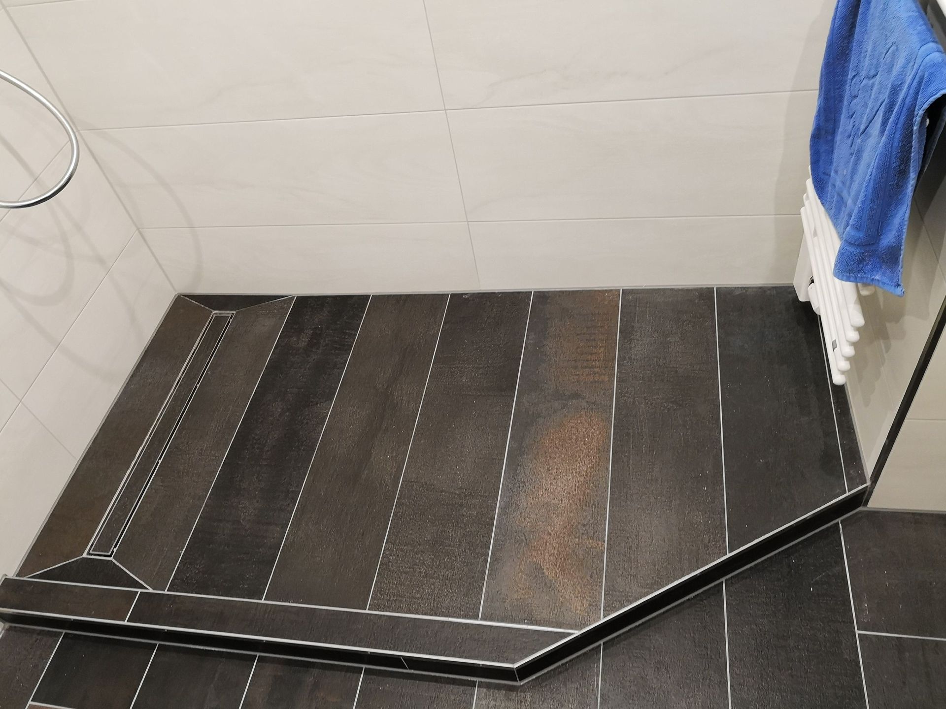 Ein Badezimmer mit ebenerdiger Dusche und einem blauen Handtuch, das an der Wand hängt.