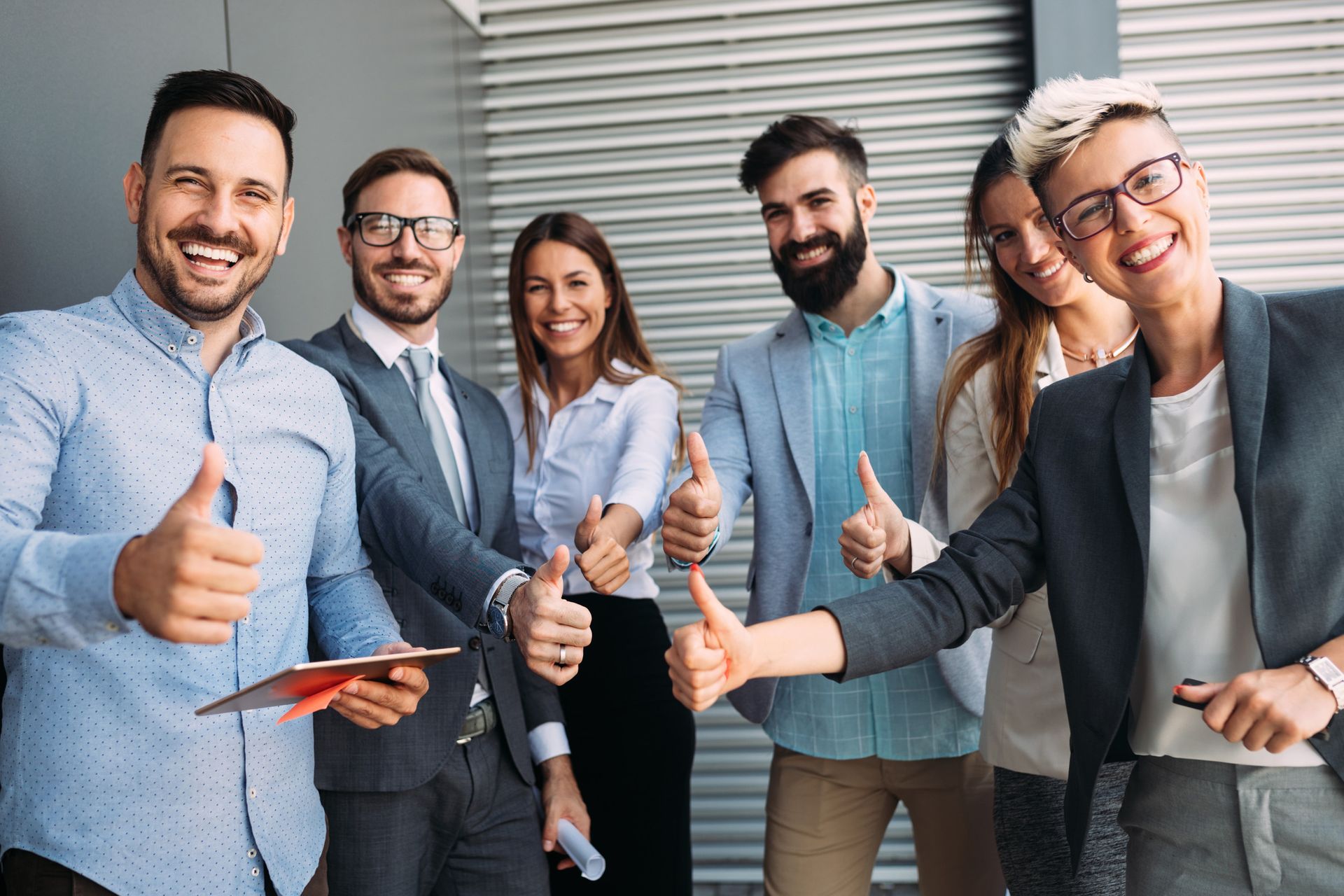 Grupo de seis profesionales sonrientes, dando pulgares hacia arriba, de pie afuera de un edificio.