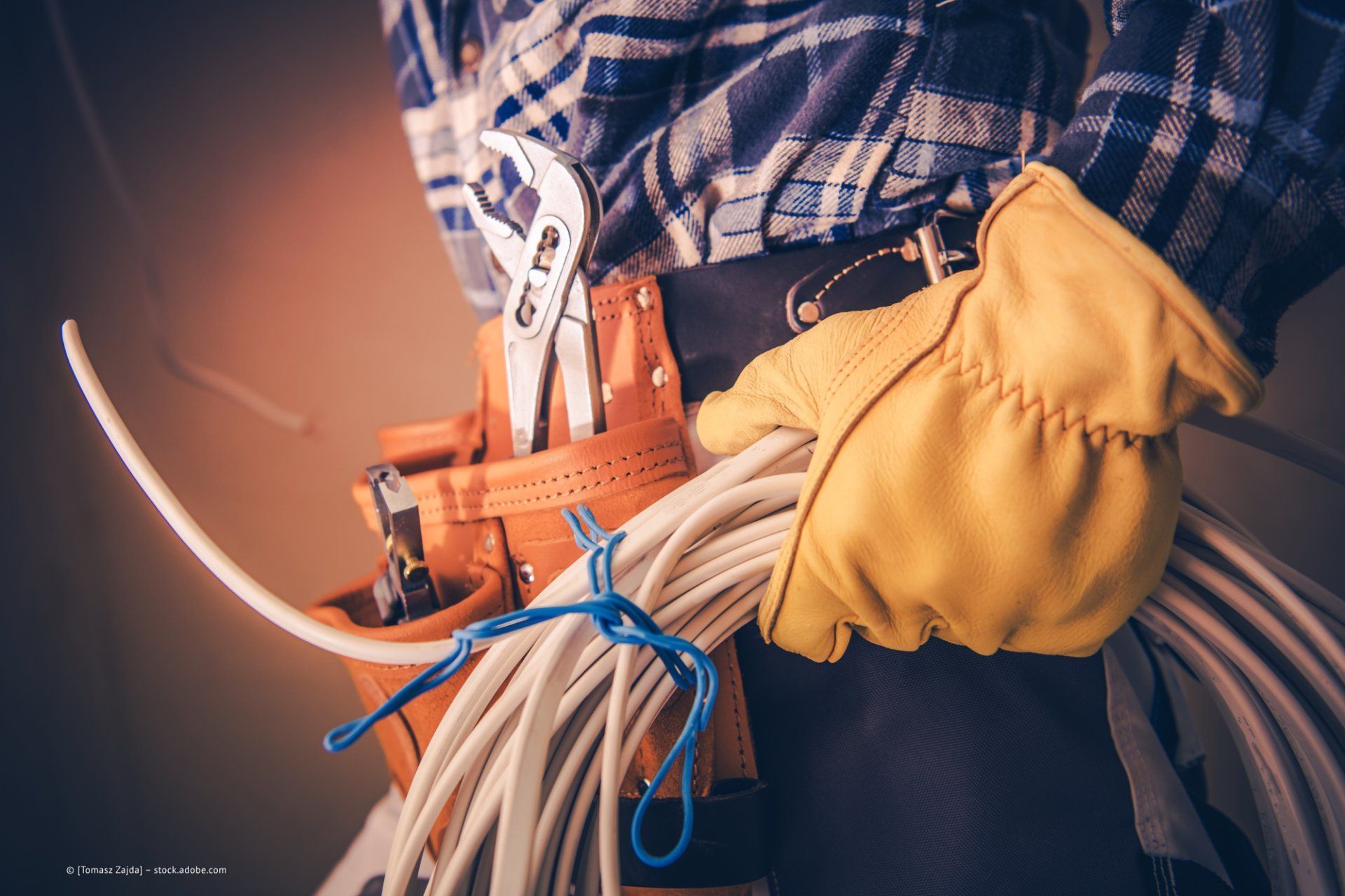 Arbeiter mit dickem gelbem Handschuh, hält eine Kabelrolle, Gürtel mit Werkzeug