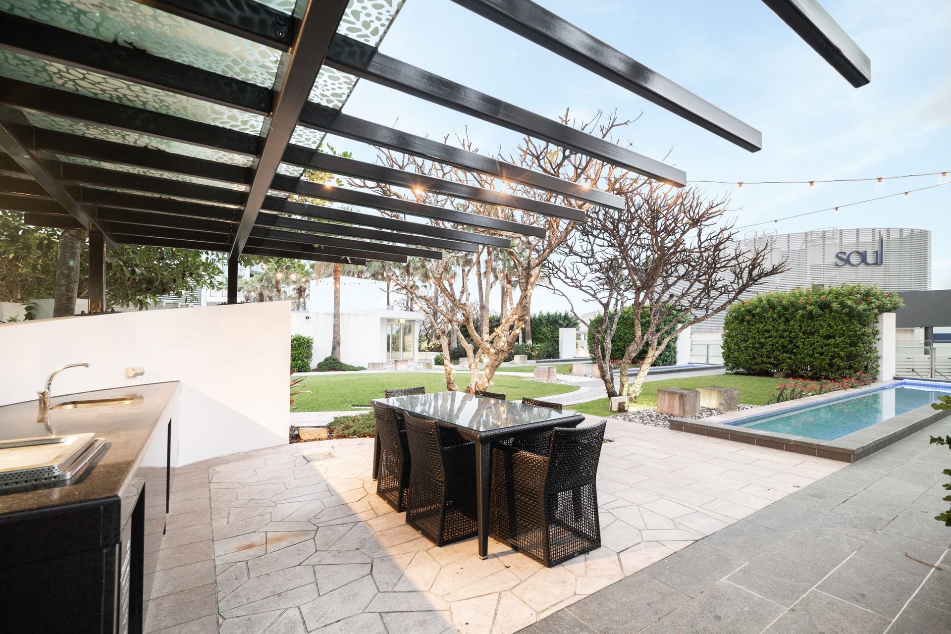 A patio with a bbq area and a table and chairs under a pergola next to a pool.