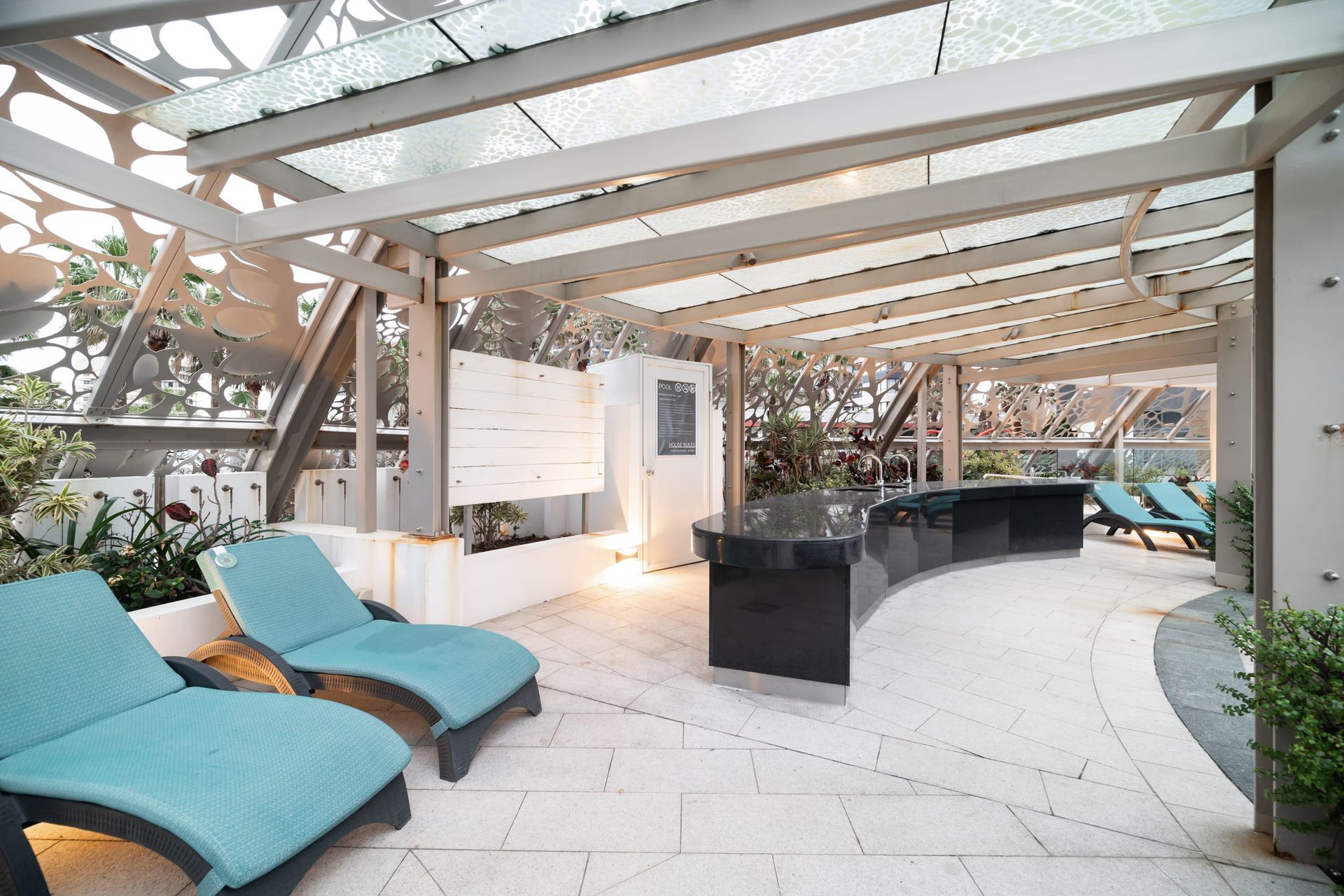 A patio with chairs and a table under a glass roof.