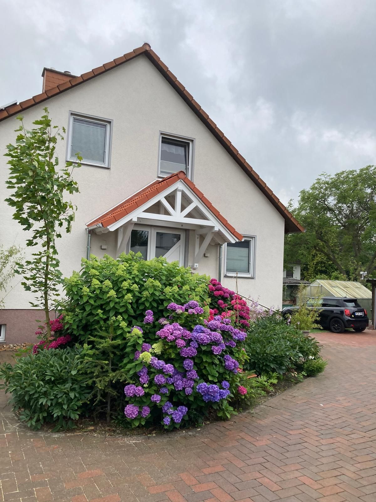 Haus mit weißer Fassade, rotem Dach und bunt blühenden Hortensien im Vorgarten.