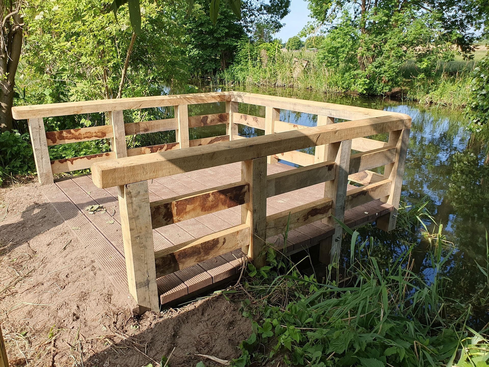 Holzplattform mit Geländer und Blick auf ein Gewässer in natürlicher Umgebung.