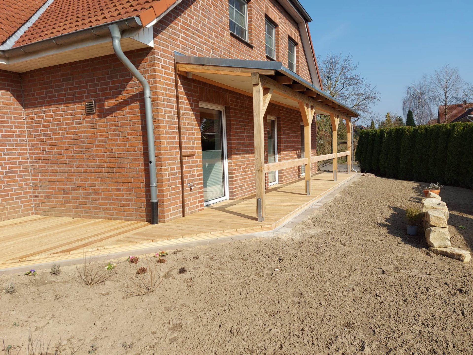 Hölzerner Verandaanbau an einem Backsteinhaus mit Geländer und Dach und Kiesplatz.