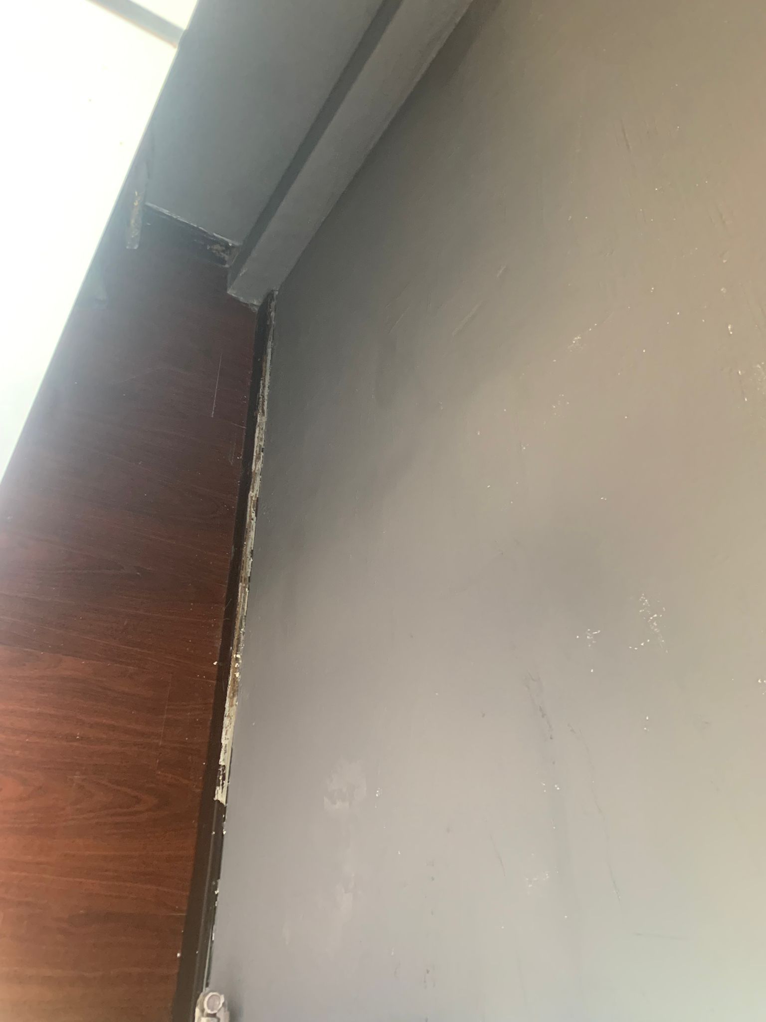 Primer plano de la esquina de una pared con molduras desconchadas junto a un marco de puerta de madera oscura.