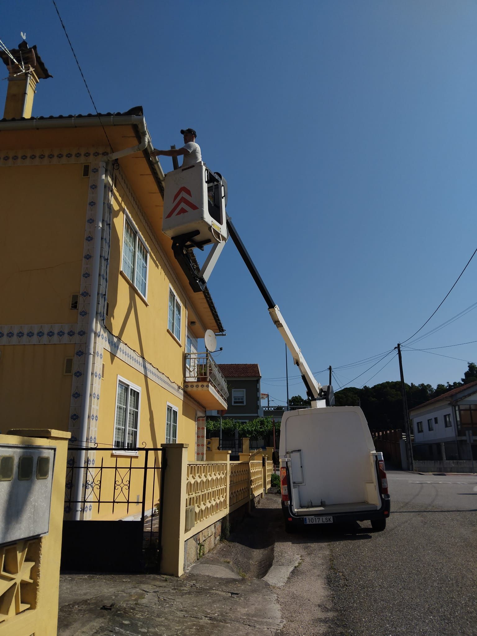 Un trabajador repara un edificio amarillo en una calle soleada subido a una plataforma elevadora