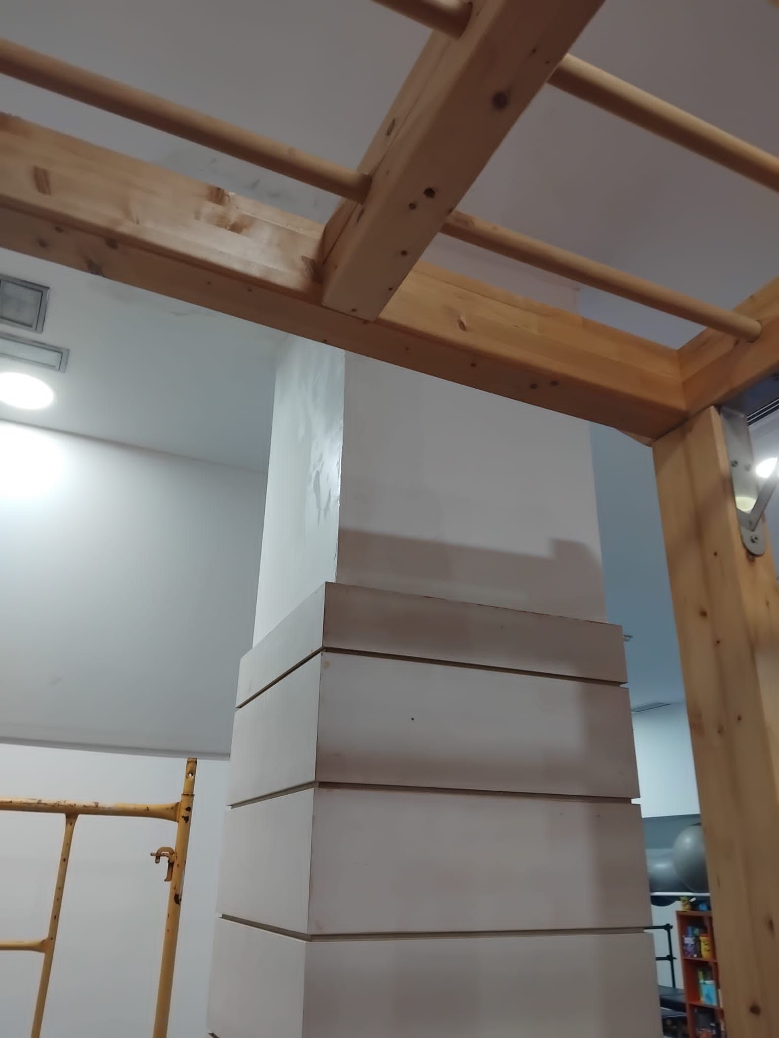 Habitación interior con cajas blancas apiladas alrededor de un pilar central bajo un marco de techo de madera.