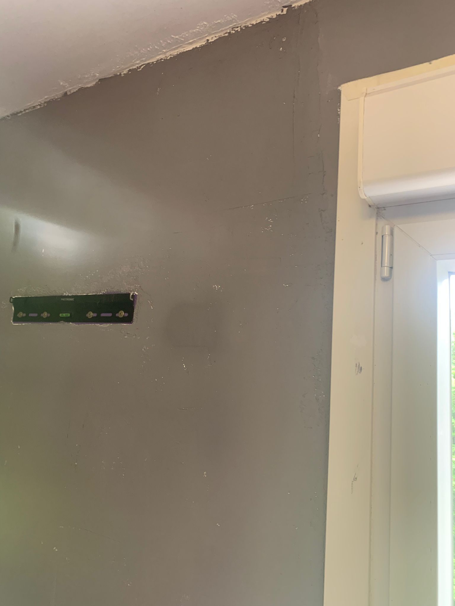 Pared pintada de gris con un nivel verde montado junto a un marco de puerta y moldura de ventana blancos.