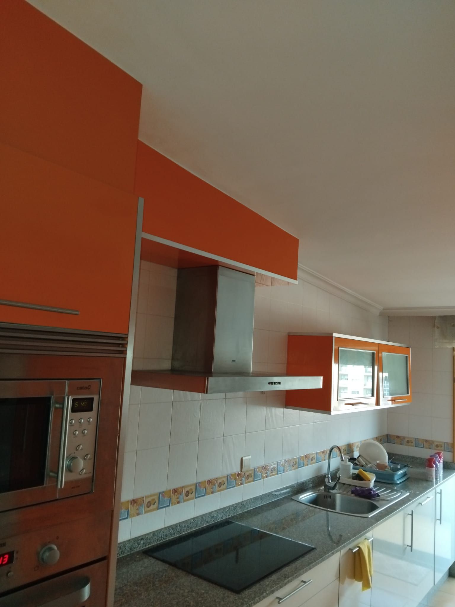 Cocina moderna con gabinetes naranjas, campana extractora de acero inoxidable, estufa, fregadero y ventana sobre la encimera.