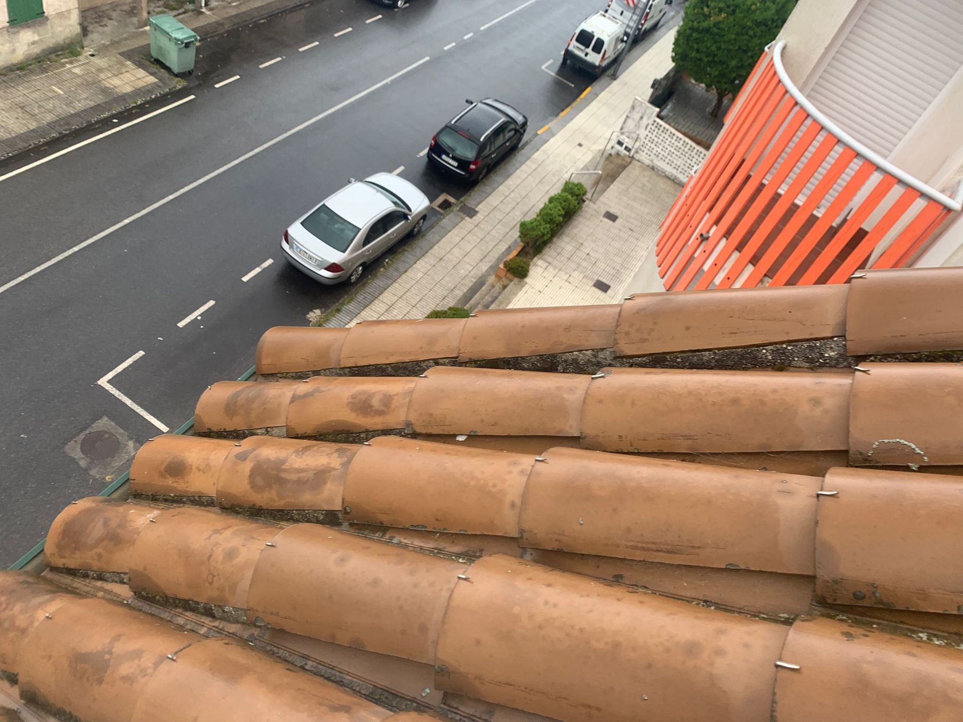 Vista desde una azotea con tejas que da a una calle con coches aparcados junto a un edificio y una acera.