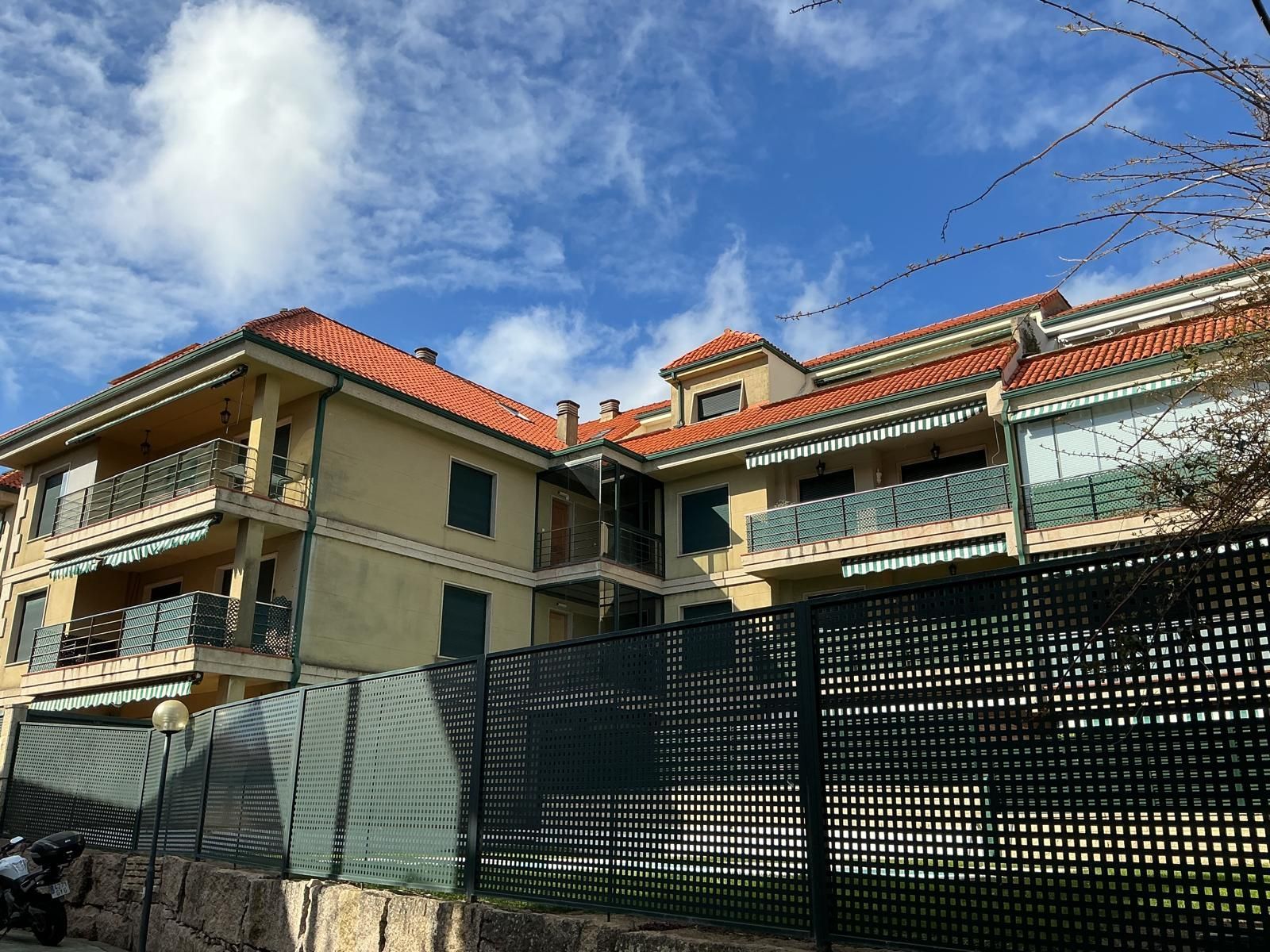 Edificio residencial con tejados de tejas rojas detrás de una valla de metal oscuro bajo un cielo azul claro.