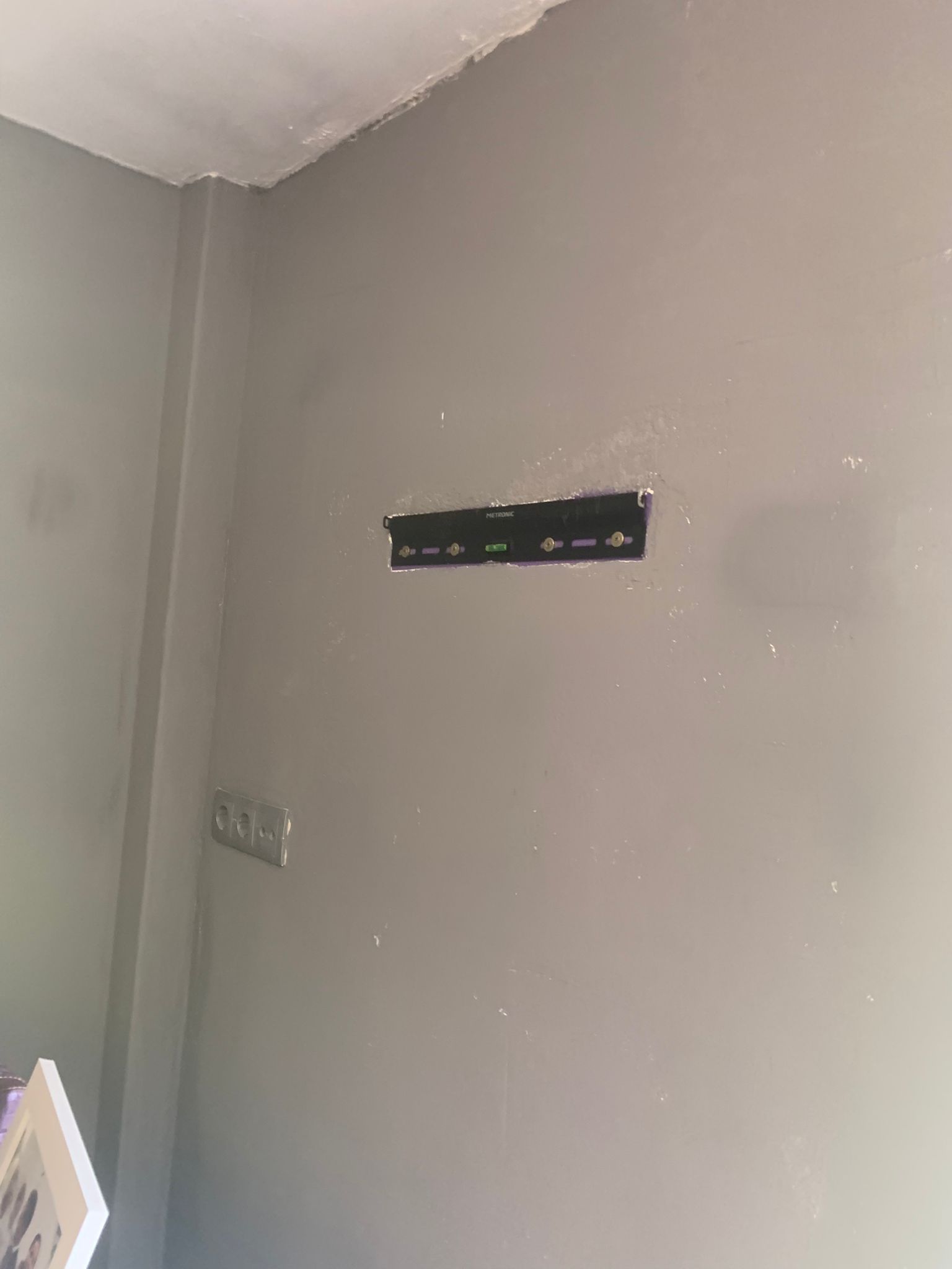 Pared gris de la habitación con un soporte negro montado en la pared y una placa de interruptor de luz cerca de la esquina.