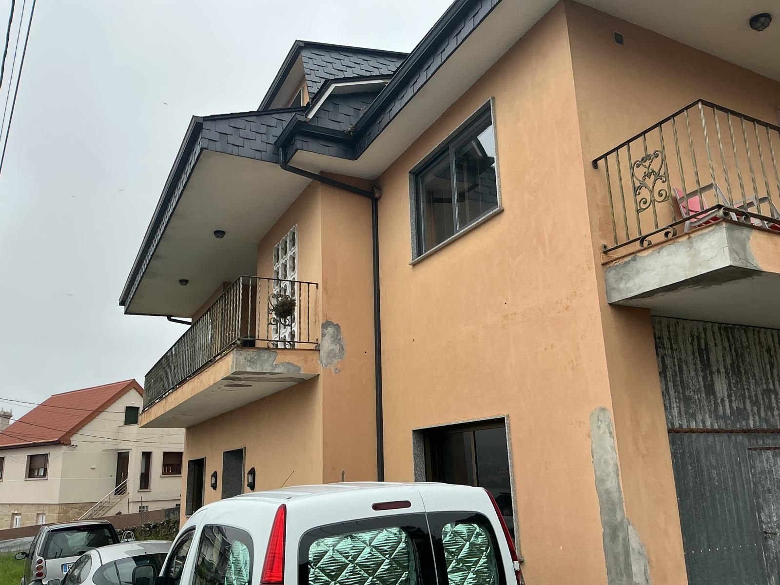 Casa de dos plantas color melocotón con balcones y una furgoneta blanca aparcada delante.