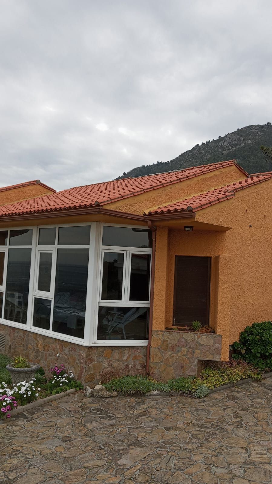 Casa de estuco con techo naranja, ventanas blancas y un camino de piedra bajo un cielo nublado.