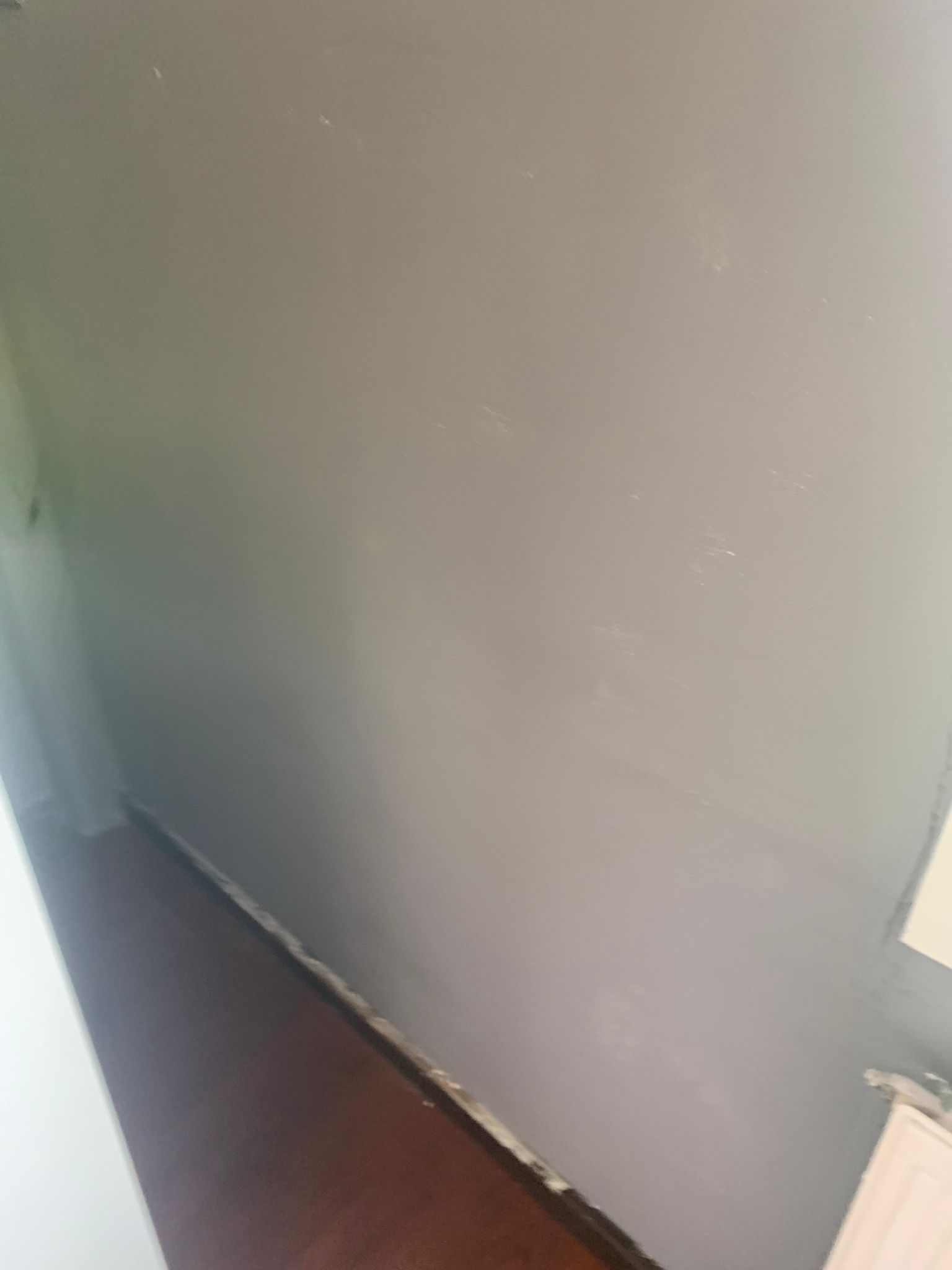 Pared gris vacía junto a un suelo de madera oscura y un rodapié blanco, con un radiador a la derecha.