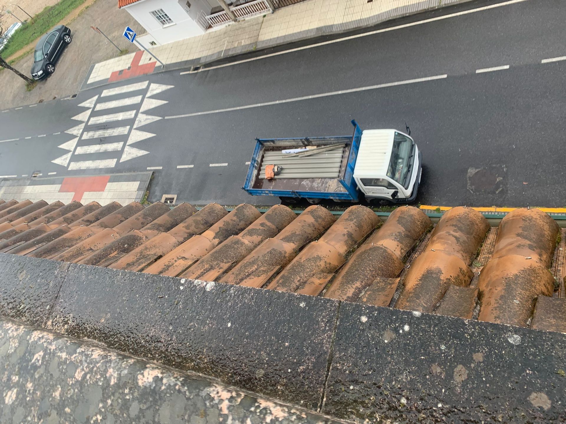 Un camión circulando por una calle mojada junto a un paso de peatones, visto desde una azotea.