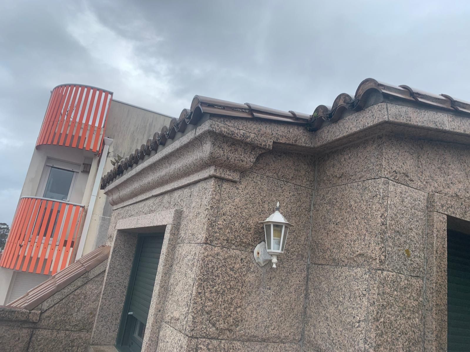 Edificio de piedra en esquina con un elaborado remate de techo y una linterna blanca en la pared bajo un cielo nublado.