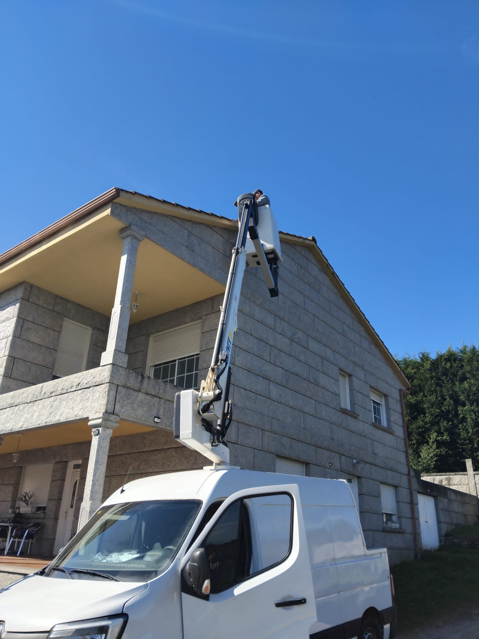 Un trabajador en una carretilla elevadora repara el piso superior de una casa bajo un cielo azul despejado.