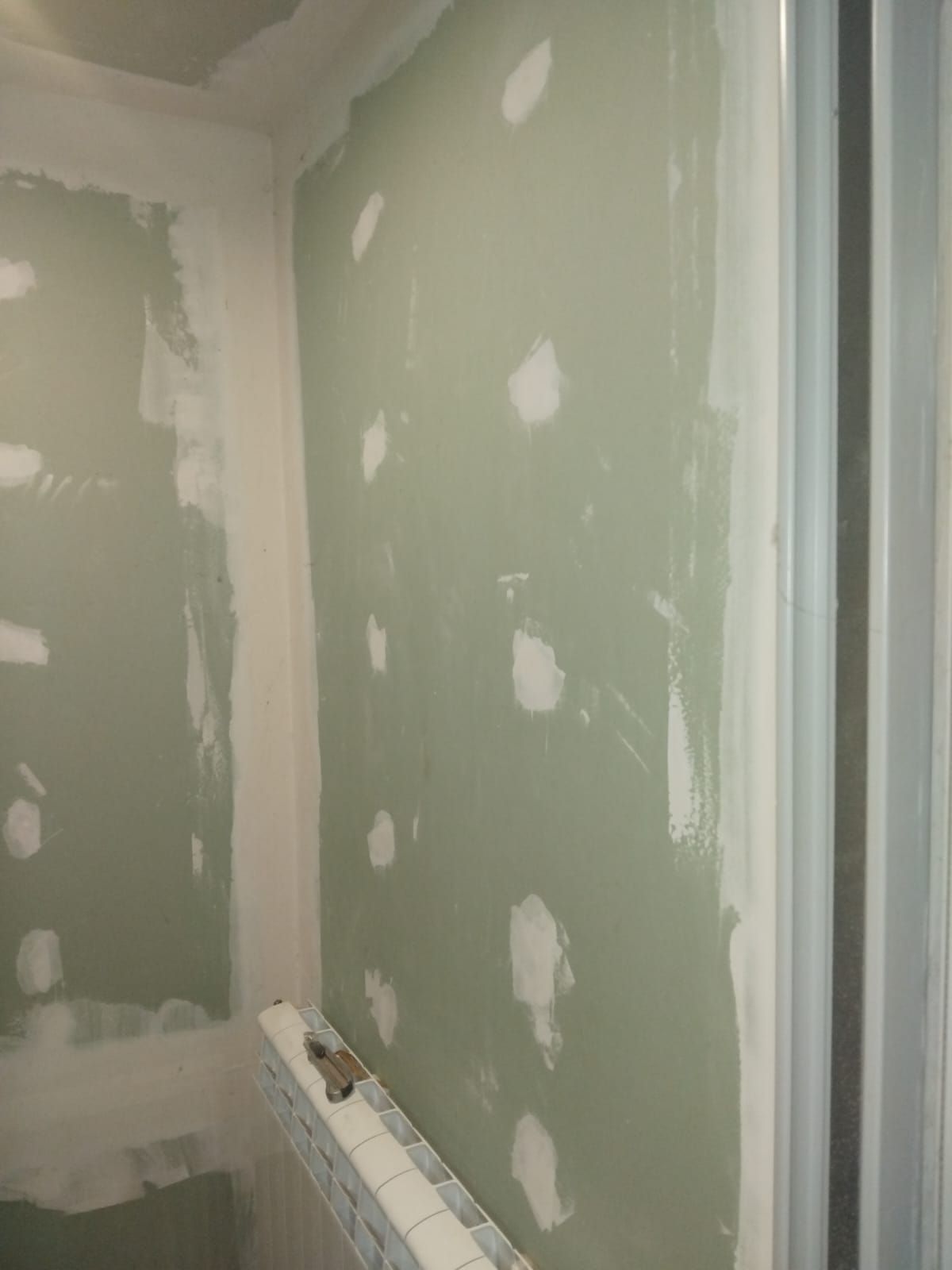 Rincón de habitación sin terminar con parches de yeso verde y un radiador debajo de la pared.